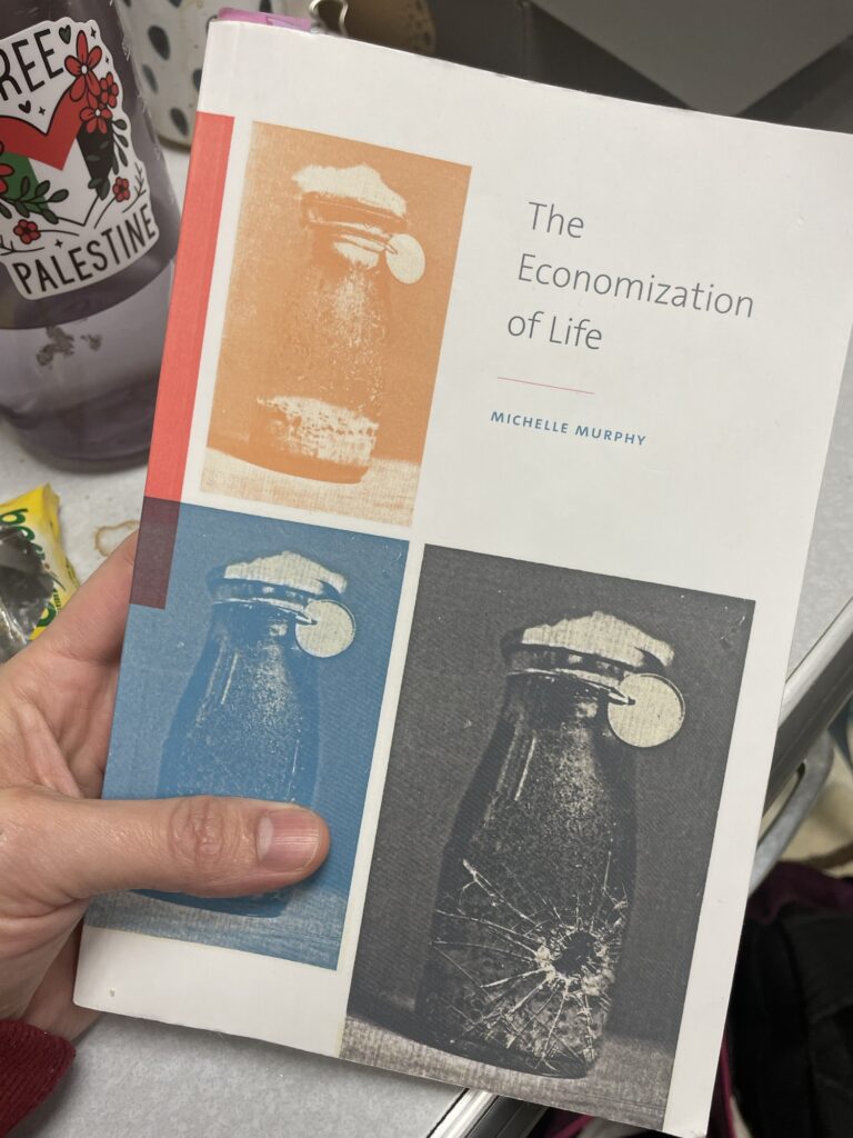 Hand holding the book, Economization of Life. Book's cover has three jars.